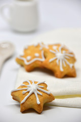 Homemade star-shaped cookies with white icing. A white spoon and a white saucer in the background.