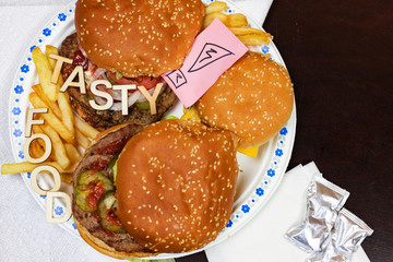 Juicy burgers and fries on a paper plate with words TASTY FOOD on burgers.