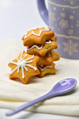 A stack of star-shaped cookies with white icing. Purple spoon and a purple cup with winter ornaments in the background.