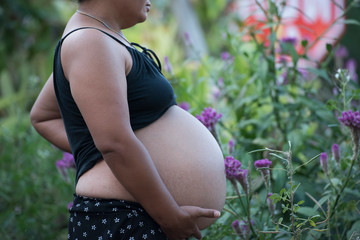 Young pregnant woman embracing her naked abdomen with hands outdoor. Big belly on the third...