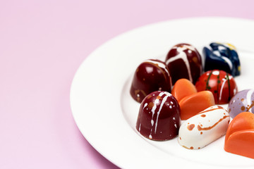 Luxury Bonbons Painted with Differents Colors on White Plate on Pink background Beautiful and Exclusive Handmade Chocolate Candy