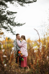 Fototapeta premium Couple in love walks through autumn forest. Hugs and kisses of men and women, relationships and love. Young couple stands in yellow red grass, a bouquet of flowers in girl hand