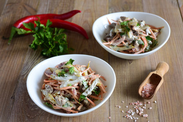 Spicy salad with meat, cucumbers and carrots in Korean in a white plate on a wooden table