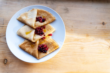 Russian tradition homemade pancakes with berries are on white place on wooden background with sunlights. Maslenitsa concept, russian festival