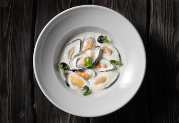 Cooked mussels with white cream sauce, herbs in a plate. Close-up, top view, on a wooden background.
