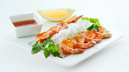 King prawns with white rice on a white plate with sauce, lemon and parsley. Isolated