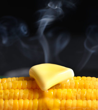 Ear of corn with melting butter and steam. Large, dark background.