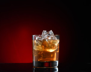 A glass of scotch tape, whiskey, bourbon with ice cubes. Dark background with red, horizontal