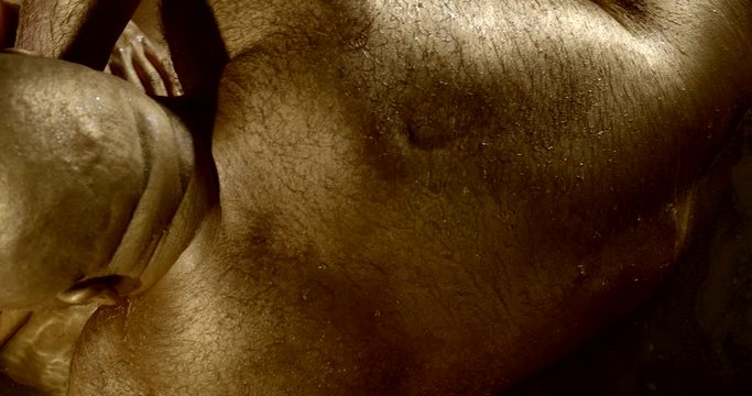 close-up of a man lying on a woman in the water. two naked bodies covered with gold paint gently touch each other