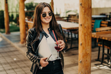 Photo of young caucasian female walking on street on a sunset time with a laptop in her hand.