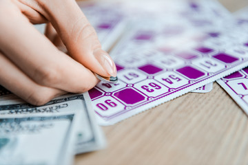 cropped view of woman holding coin and scratching lottery ticket on table