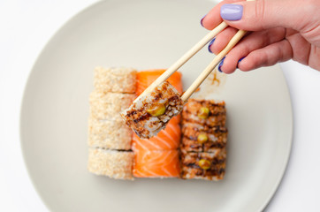 A girl holds a roll with chopsticks.