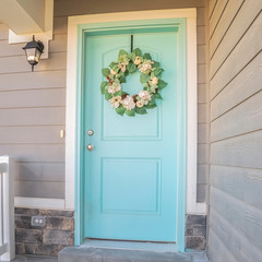 Square frame Wooden blue front door with wreath on a sunny day