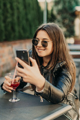 Young woman making self portrait using smartphone. Girl making selfie. Woman in cafe. Woman alone. Self portrait in cafe outdoors. smile. smilimg. gadget. self portrait. coffe break. coffee time