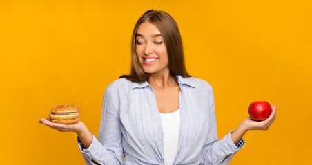 Girl Choosing Burger Instead Of Apple Standing On Yellow Background