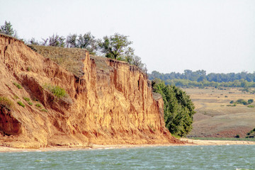 A steep shore, sandy cliff near a deep lake.