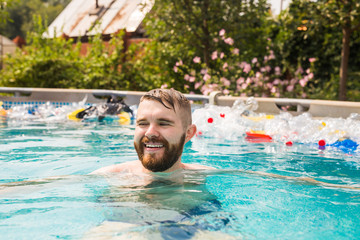 Problem of trash, plastic recycling, pollution and environmental concept - silly man swim and have fun in a polluted pool. Bottles and plastic bags float near them