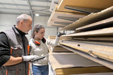 Carpenter in warehouse giving instructions to apprentice