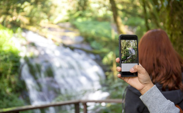 Women's hands using a tablet to take a photo of an exotic waterfall in a tropical rain forest.