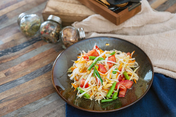 Traditional Thai food papaya salad prepared with fine slices of papaya, tomatoes, green beans and peanuts.