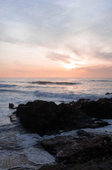 Fototapeta premium Sunset over the ocean, waves break down to rocks in the water