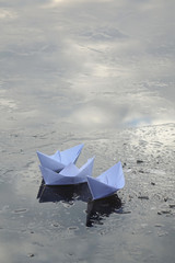 three paper boats sail on frozen water