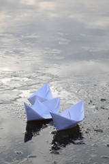 three paper boats sail on frozen water
