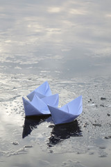 three paper boats sail on frozen water