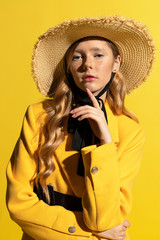 Pretty blonde girl with freckles in yellow outfit and straw hat on yellow background