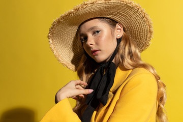Pretty blonde girl with freckles in yellow outfit and straw hat on yellow background
