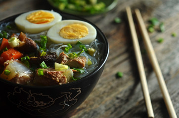 Asian chicken soup with noodles and egg in a black bowl on a wooden background