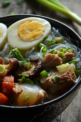 Asian chicken soup with mushrooms and egg in a black bowl on a wooden background