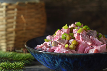 Herring salad with peas in a blue bowl on a wooden background
