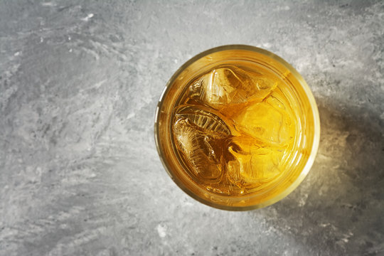 Top View Of Whiskey With Ice In A Glass On A Gray Concrete Background, Close-up. Overhead