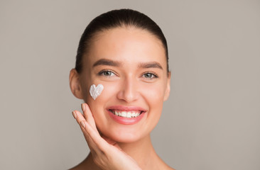 Skin hydration. Positive girl applying moisturizing cream on cheek