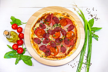 pizza with sausages and ham, olive oil and basil on a white background, flat lay