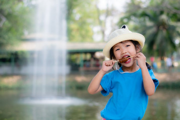 An Asian girl is standing eating ice cream by the pool.