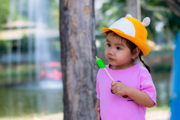 An Asian girl is standing eating ice cream by the pool.