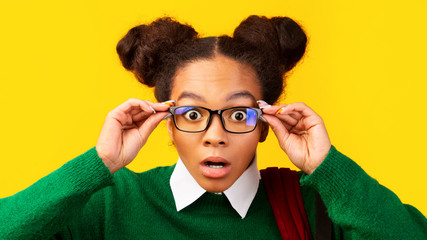 Amazed afro teenager with opened mouth touching glasses