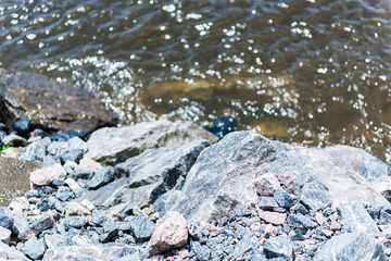 Colorful rocks on Saint Laurent or Lawrence river in Quebec, Canada during summer with brown water