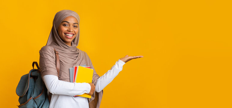 Cheerful black islamic female student in hijab pointing aside with hand