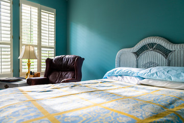 Low angle view of clean bed vintage beach theme decorative blue pillows in bedroom home, house or apartment by red leather couch and sunlight windows