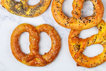 Pretzel. A set of different pretzels with black and white sesame, poppy seeds, cumin or caraway, large sea salt on a marble table. Sweet and salty appetizer. Selective focus