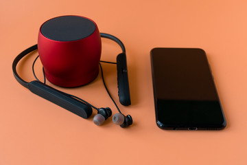 Wireless devices for the phone, black headphones and a red speaker. Headset for phone on an orange background.