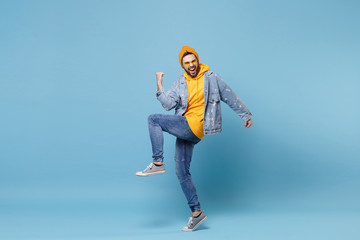 Laughing young hipster guy in fashion jeans denim clothes posing isolated on pastel blue wall background studio portrait. People emotions lifestyle concept. Mock up copy space. Doing winner gesture.