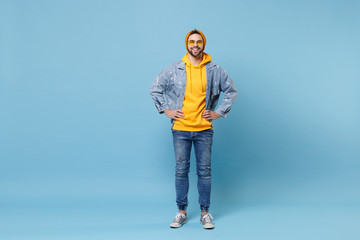 Smiling young hipster guy in fashion jeans denim clothes posing isolated on pastel blue background...