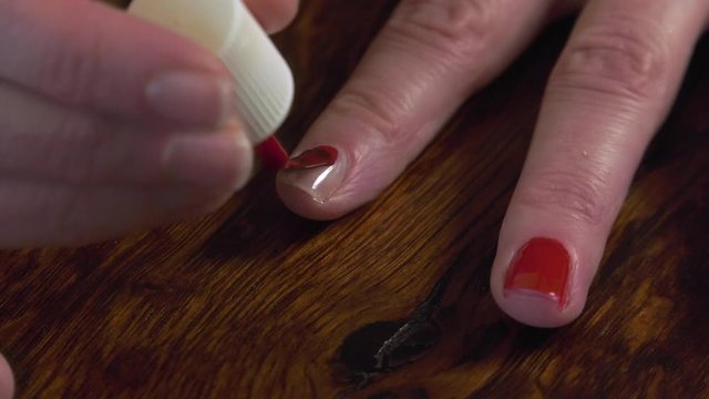 Woman applies bright red nail polish to her unpainted fingernail. Close-up shot of two fingers with fresh nail polish.