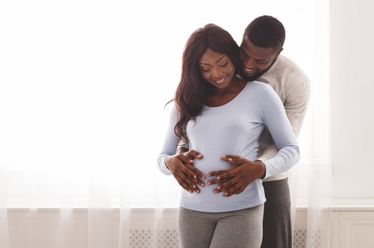 Pregnant smiling black woman and her husband cuddling at home