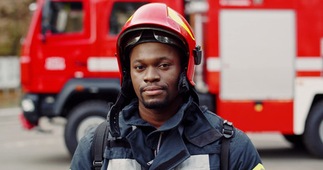 Portrait of african american brave fireman standing near fire truck