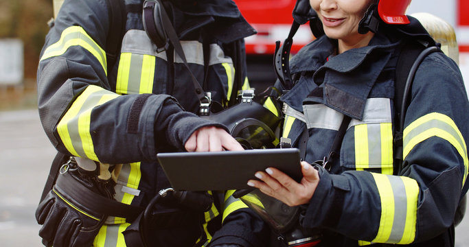 Portrait of two firefighters in fire fighting operation, fireman in protective clothing and helmet using tablet computer in action fighting. - Powered by Adobe